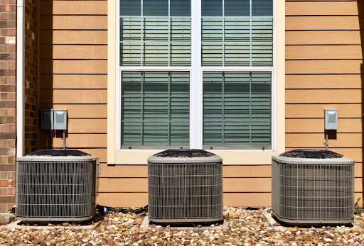 Three central air conditioner compressor units outside of a residential building.