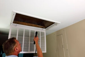 A man using a flashlight to inspect an air vent.